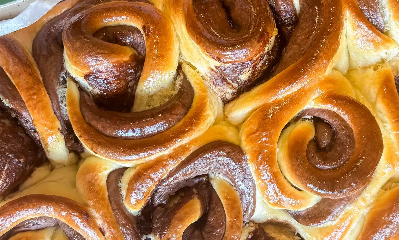 Čokoladne ružice od tijesta tople zlatnosmeđe boje s tamnim, sjajnim čokoladnim spiralama na svijetloj podlozi u plehu.