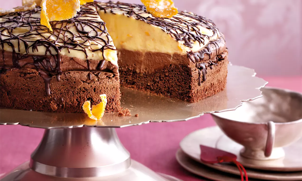 Čokoladno-narančasta torta s tamnom biskvitnom podlogom, slojem žute kreme, čokoladnim preljevom i ukrasima od narančine korice na srebrnom stalku