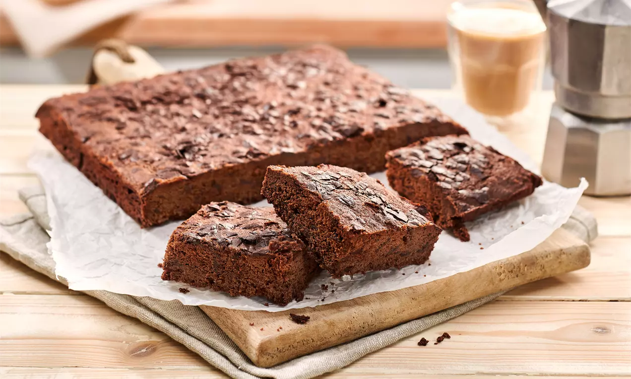 Čokoladni brownies kvadratnog oblika, tamnosmeđe boje s hrskavom površinom, posloženi na papiru za pečenje na drvenoj podlozi