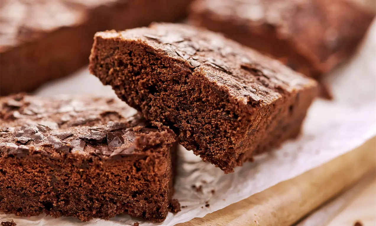 Čokoladni brownie u tamnosmeđim nijansama s lagano ispucalom koricom i mekanom unutrašnjosti na papiru za pečenje