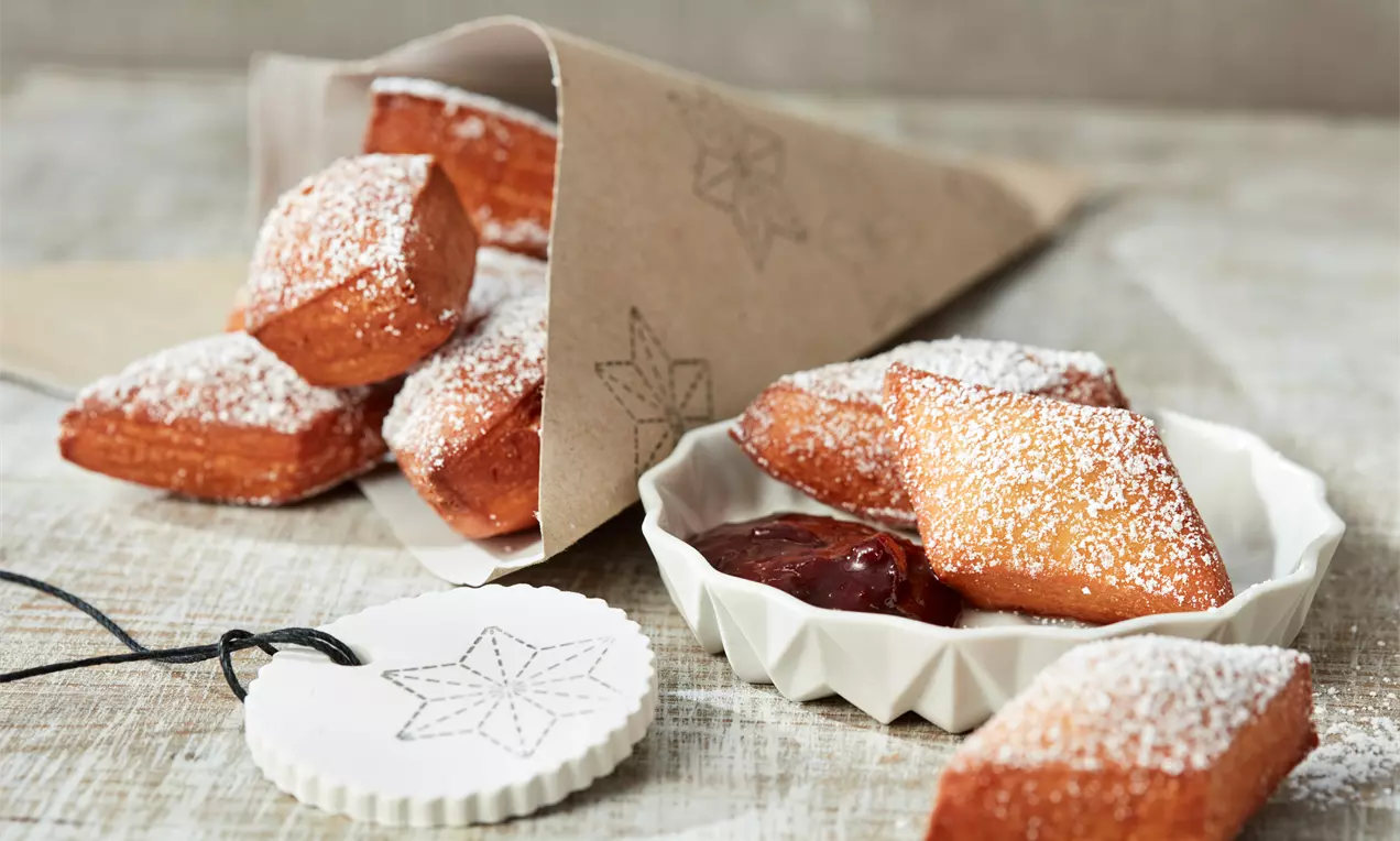 Zlatnosmeđi Schmalzkuchen u obliku kvadrata posut šećerom u prahu, raspoređen u papirnatom fišeku i keramičkoj posudi s džemom.