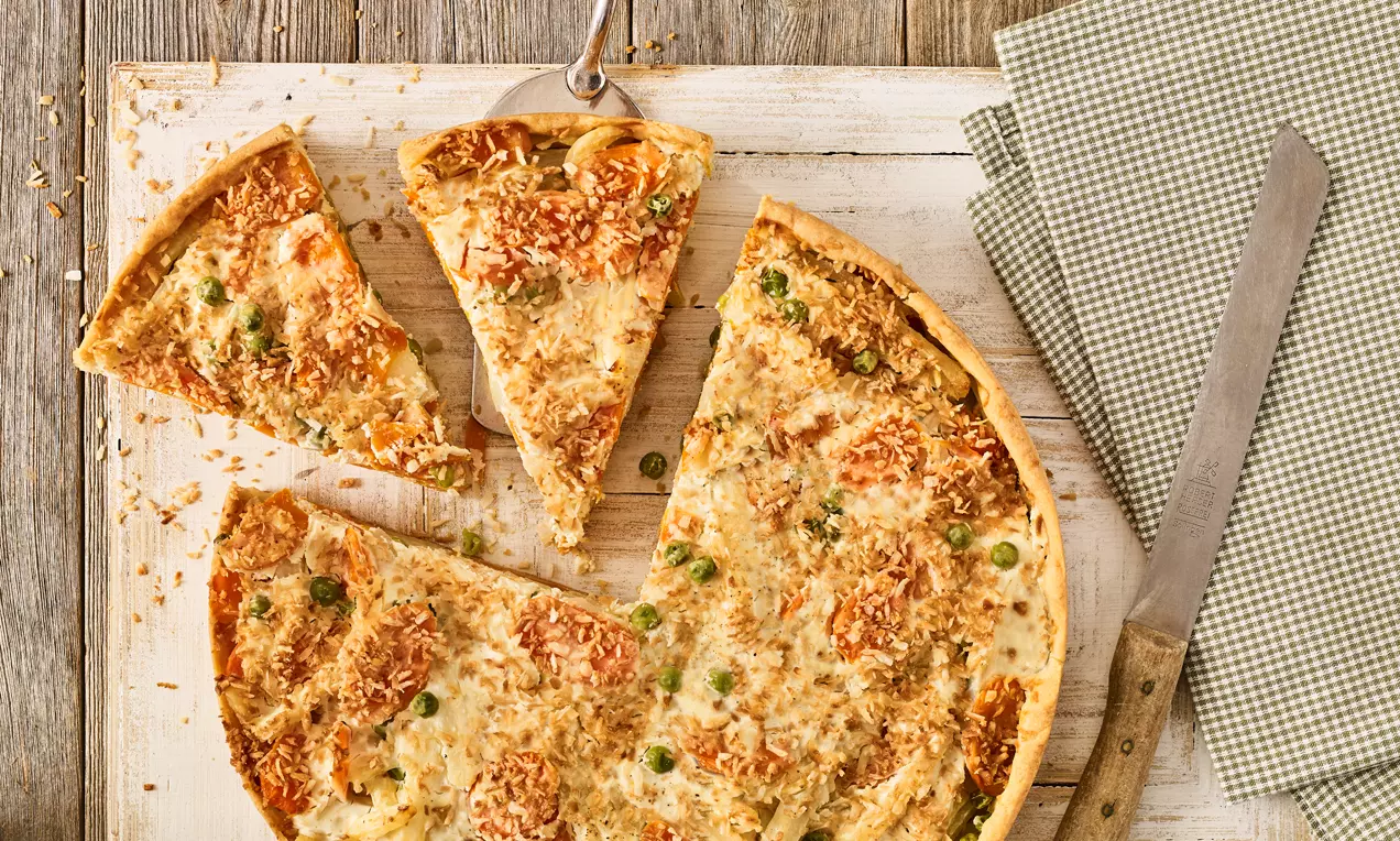 Veganska quiche svijetlosmeđe kore, posuta zapečenim komadićima povrća i hrskavim mrvicama na drvenoj podlozi uz zelenu tkaninu