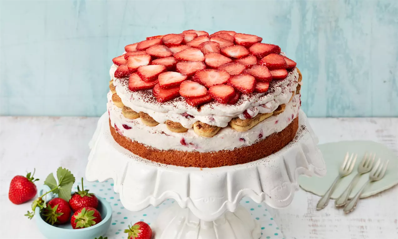 Torta u slojevima s bazom zlatnosmeđeg biskvita, kremom i savoiardi keksima, ukrašena svježim ploškama jagoda na bijelom postolju