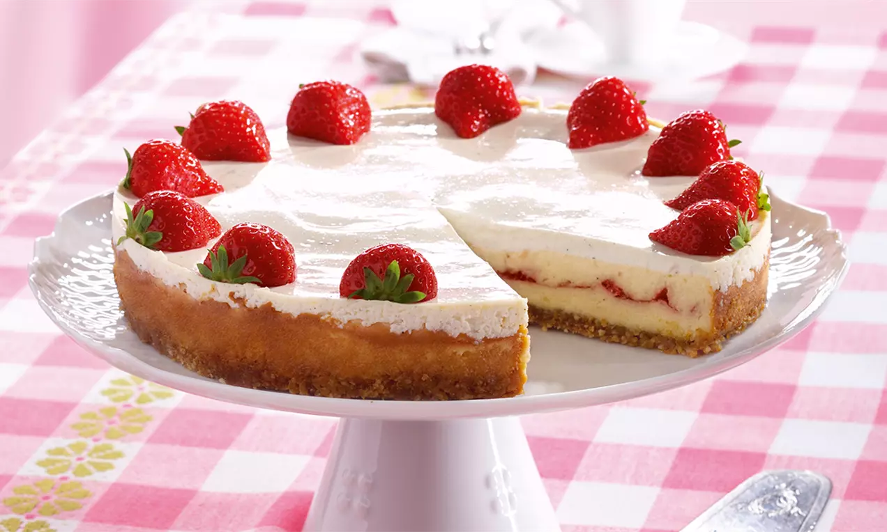 Kremasta torta na svijetloj podlozi s debelim slojem bijele kreme, svježim cijelim jagodama na vrhu i slojem zlatnosmeđe baze