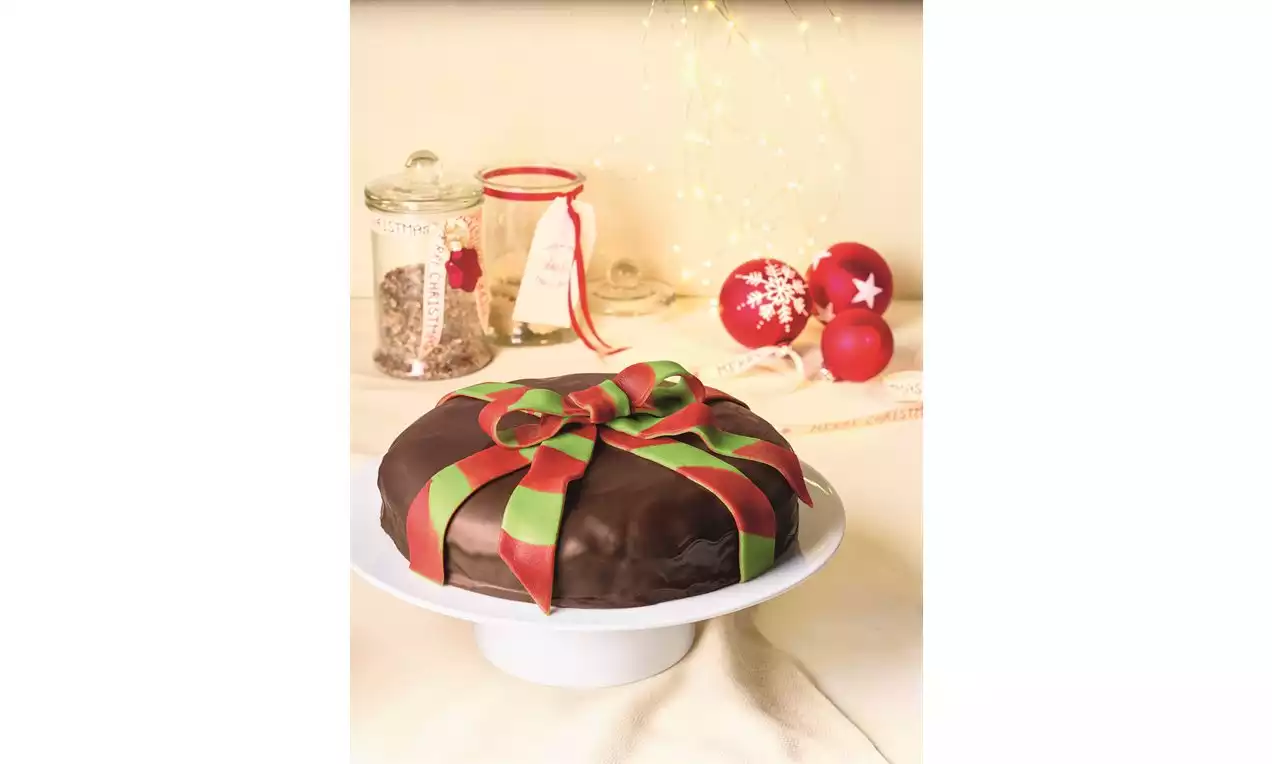 Božićna torta s glatkom čokoladnom glazurom i dekoracijom od crveno-zelenih trakica oblikovanih u veliki mašni na bijelom stalku