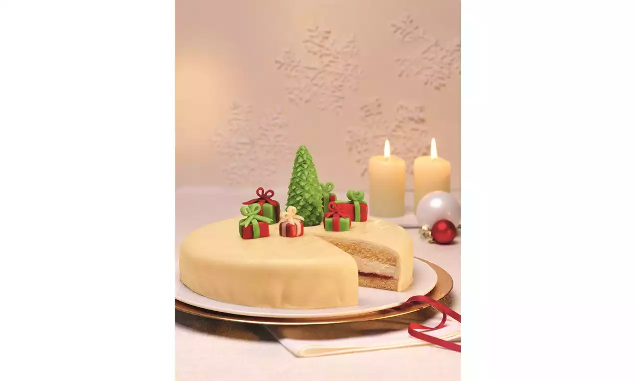 Božićna torta s glatkom bež glazurom, prerezana kako bi otkrila svijetlu unutrašnjost, ukrašena zelenom jelkom i šarenim darovima