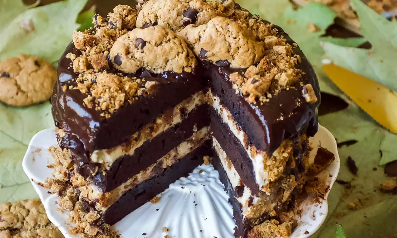 Čokoladna torta s tamnim slojevima biskvita, kremastim punjenjima, preljevom od čokolade, posuta mrvicama keksa i ukrašena cijelim keksima.